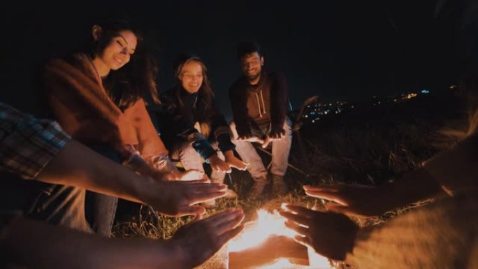 朋友们坐在夜晚篝火旁，暖手