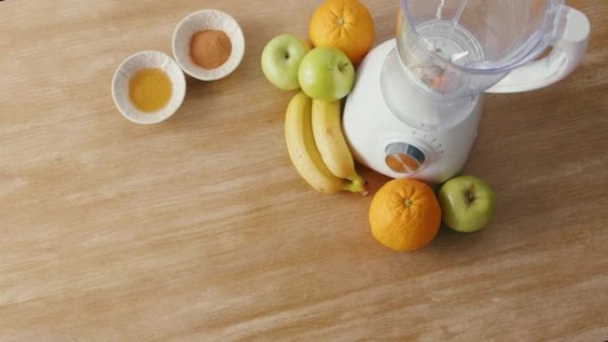 木制桌子上出现的新鲜农产品和其他健康奶昔成分的俯视图。水果，杏仁和配料以及用于制作冰沙的搅拌机。健康