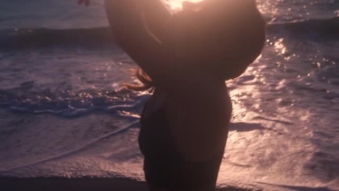 日落时在海滩上跳舞的年轻女子的剪影