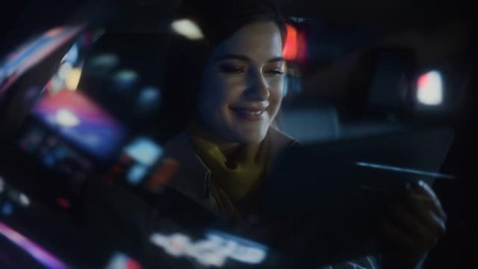 时尚的女性晚上坐出租车后座回家。美丽的女人乘客使用平板电脑，在城市街道上开着霓虹灯，看着窗外。
