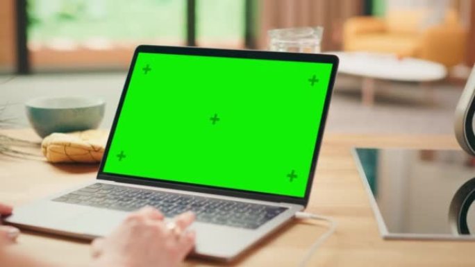 在笔记本电脑上关闭绿色屏幕模型。设备用于现代家庭的厨房桌子上。人使用触摸板滚动网页。阳光现代厨房，拥