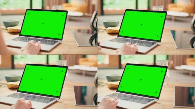 在笔记本电脑上关闭绿色屏幕模型。设备用于现代家庭的厨房桌子上。人使用触摸板滚动网页。阳光现代厨房，拥
