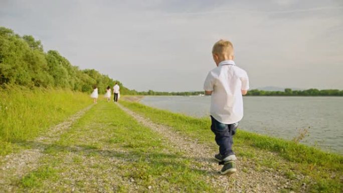 SLO MO小男孩在河边走在父母和两个兄弟姐妹的后面
