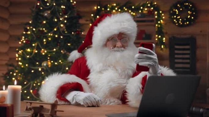圣诞老人正在用手机与某人通话，他在圣诞老人的办公室里，圣诞树在他身后