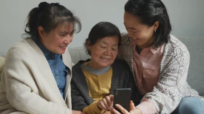 微笑的亚洲高级女性使用智能手机，成年女儿和孙女拥抱