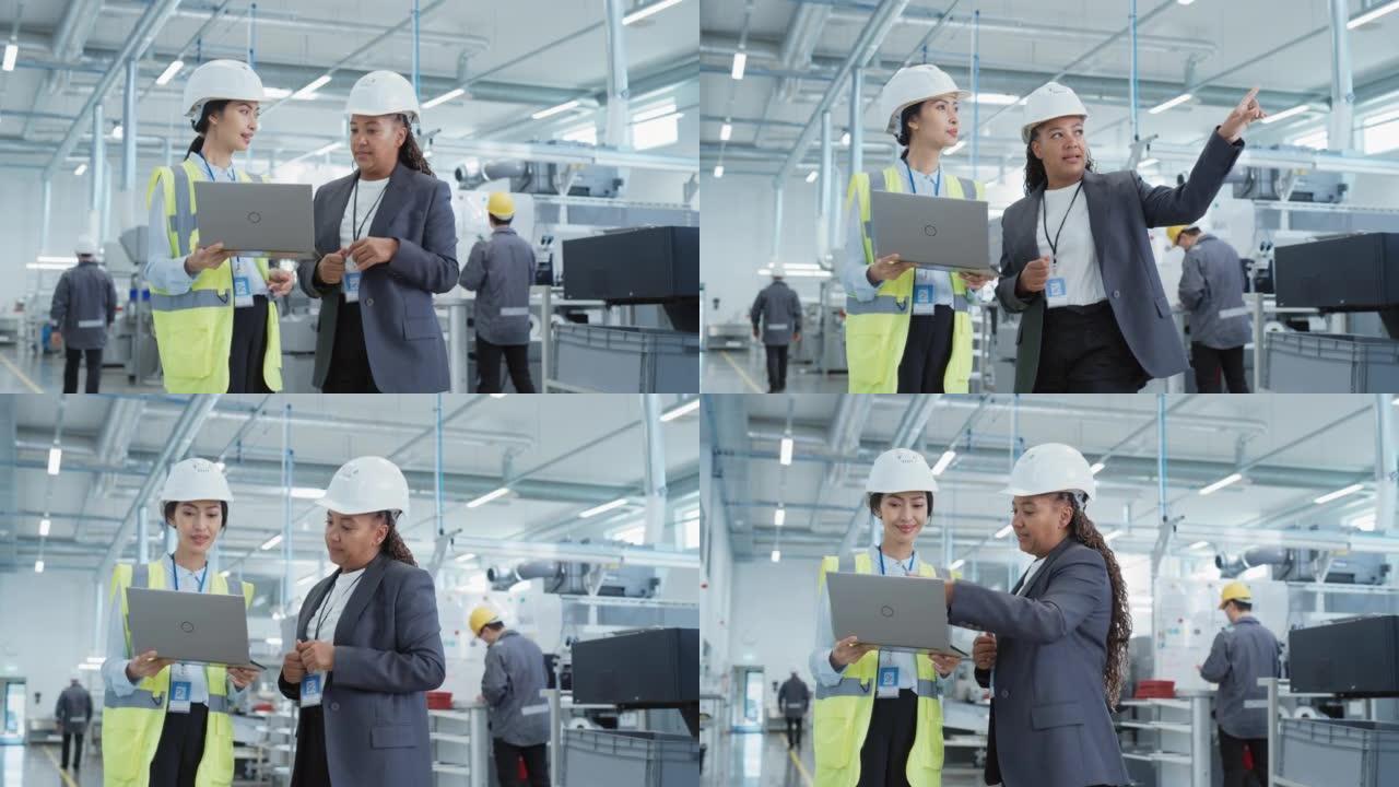 两名女重工业员工在工厂戴着安全帽。使用笔记本电脑讨论工业机械设施的工作分配。工作中的亚洲工程师和非裔