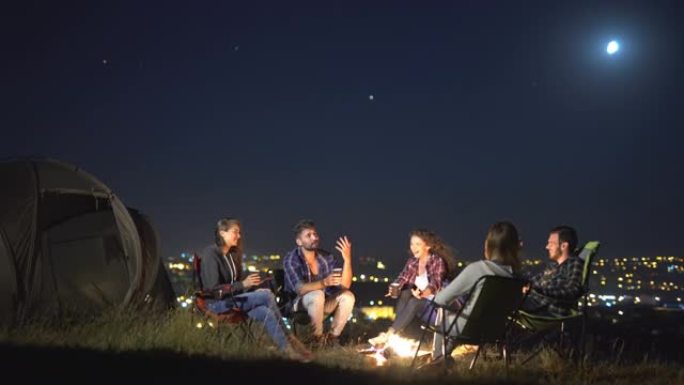 人们在夜城背景下的帐篷附近坐着聊天