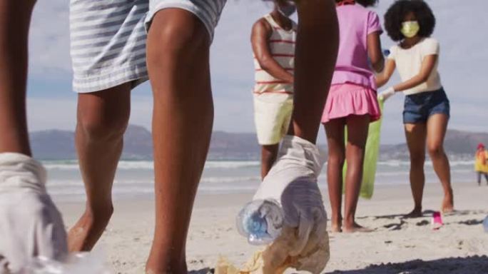 有两个孩子戴着口罩的非裔美国父母从海滩收集垃圾
