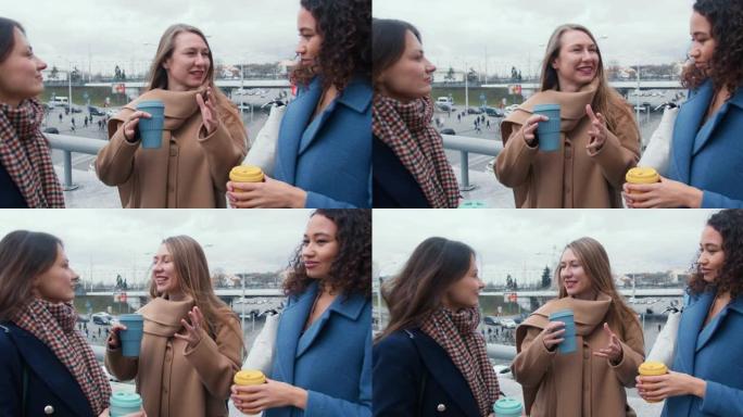 友谊和纽带。美丽的多民族年轻女性朋友在秋天的城市街道上一起喝咖啡聊天。