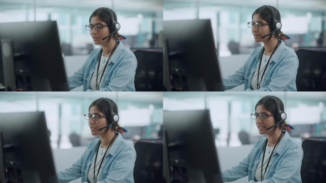 呼叫中心办公室: 友好的印度女性信息技术客户支持专家在电脑上工作的肖像。使用耳机通过在线视频电话与客