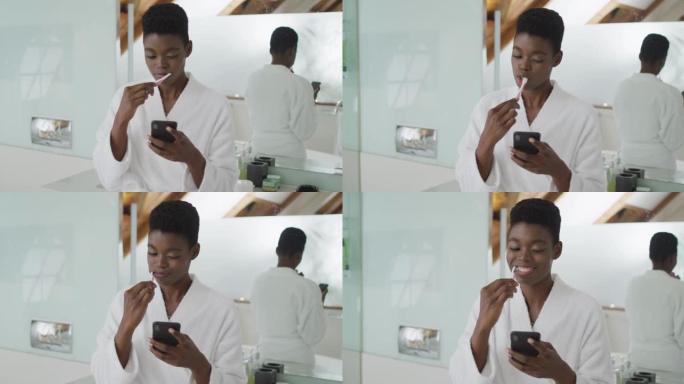 非裔美国有吸引力的女人在浴室刷牙和使用智能手机