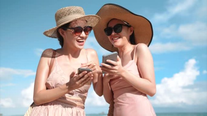 两名亚洲妇女喜欢在海滩上一起使用智能手机
