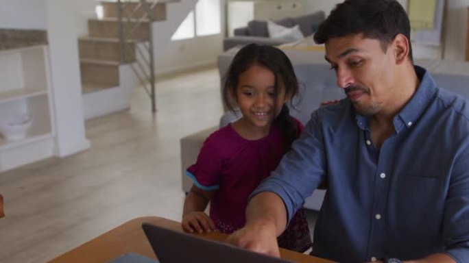 快乐的西班牙裔父亲和女儿坐在桌子旁看着笔记本电脑