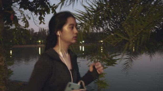 迷人的亚洲少女在公园跑步时听音乐。年轻女子在夜间慢跑锻炼。