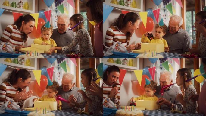 庆祝一个可爱的小男孩生日的幸福家庭肖像: 男性蹒跚学步的孩子打开礼物并拿出卡车玩具，而母亲，祖父和姐
