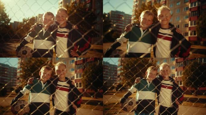 两个年轻可爱的高加索孩子的肖像，看着相机，微笑着互相拥抱。拿着足球的小男孩。夏天温暖阳光明媚的日子里
