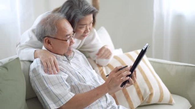 高级夫妇使用数字平板电脑进行在线购物，并在家里的客厅使用社交媒体