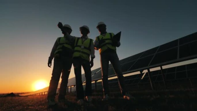 工程师团队正在讨论日落期间太阳能电池附近的一个项目。太阳能工厂附近的替代能源工人。