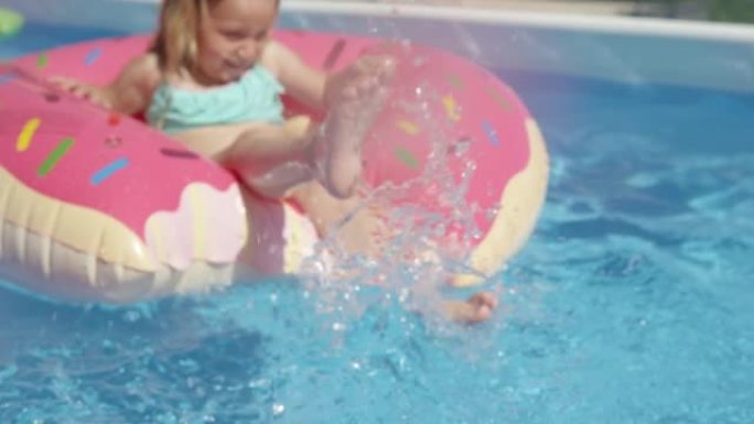 特写: 小女孩的腿从游泳池里的漂浮物甜甜圈里溅水
