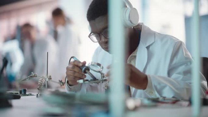 黑人男性实验室专家在一家工业公司使用耳机焊接电路板的肖像。专业人士听音乐，为一家初创公司从事技术项目