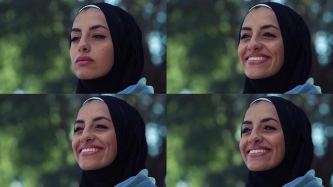 美丽的年轻阿拉伯女子微笑着绿色背景的肖像。带着头巾的快乐穆斯林女性运动员在公园享受新鲜空气，见到朋友