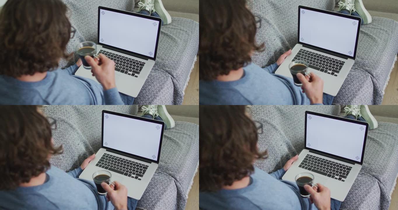 白人男子坐在客厅的沙发上，用笔记本电脑喝咖啡