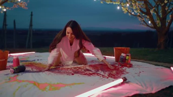 女人在后院凌乱的艺术家画布上散布水彩颜料