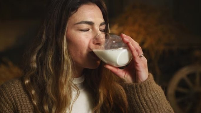 电影特写镜头，年轻的女农民喝新鲜的刚生产的生物牛奶，用于真正的乳制品行业，并在农村奶牛场的牛棚马st