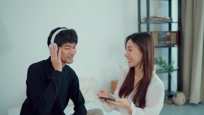 微笑的亚洲夫妇在卧室里一起用耳机休息和听音乐。