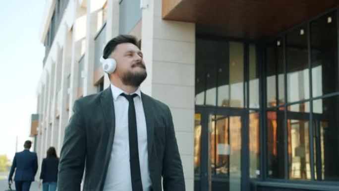 无忧无虑的商人戴着耳机在城市户外散步享受音乐的慢动作