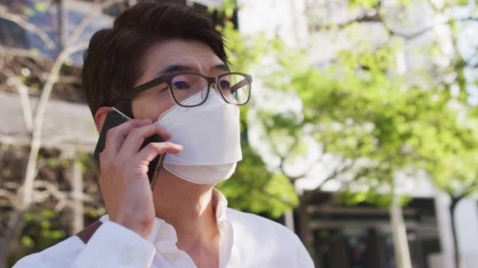 戴着口罩的亚洲男子在街上用智能手机聊天