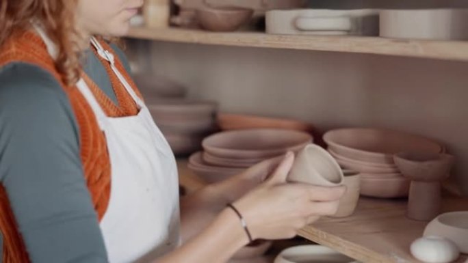陶器女人，架子和创意陶瓷杯，艺术家或工艺人员站在工匠工作室或艺术工作室。企业家波特女性喜欢在初创企业