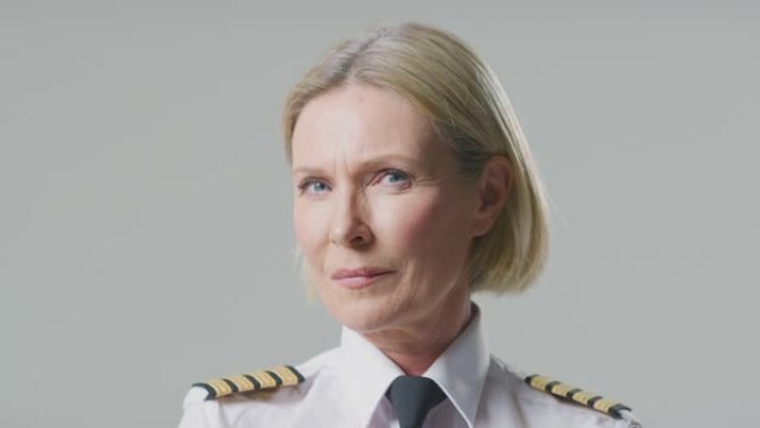 在朴素的背景下，严肃的成熟女性航空公司飞行员或船长的工作室肖像