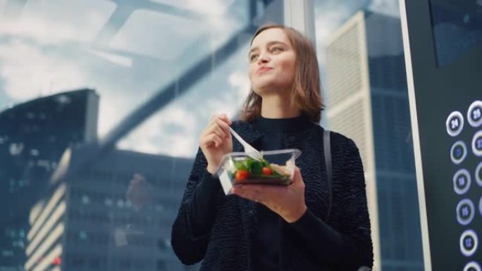 一位迷人的年轻女性乘坐玻璃电梯到现代商务中心的办公室，吃健康的蔬菜沙拉的肖像。快乐的经理为工作中富有