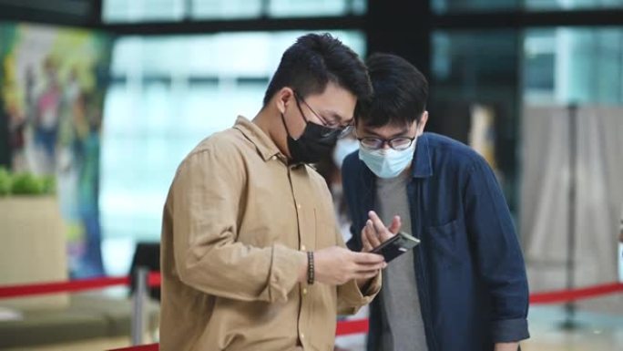 亚洲华裔年轻人在电影院前看带口罩的智能手机电影院用手机app在线电影票预订