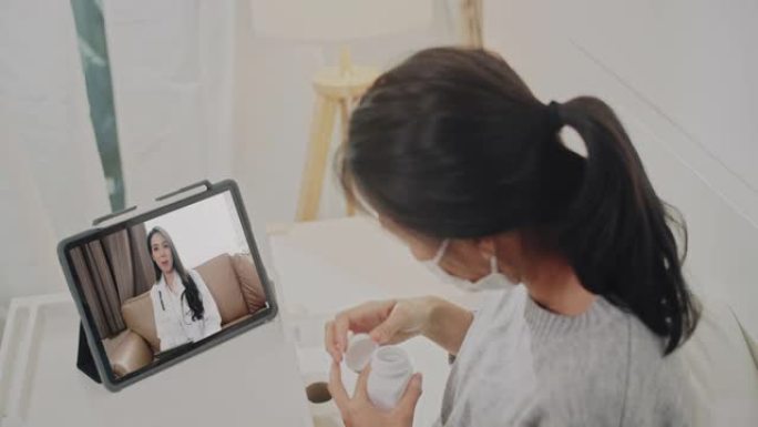 躺在坏医生身上的亚洲妇女通过在家中的视频通话，家庭保健和远程医疗概念向医生咨询药物和医疗状况