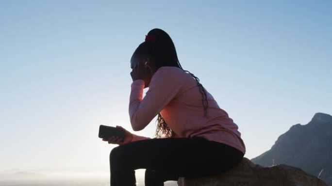 日落时分，在乡村使用智能手机坐在岩石上户外锻炼的非洲裔美国妇女