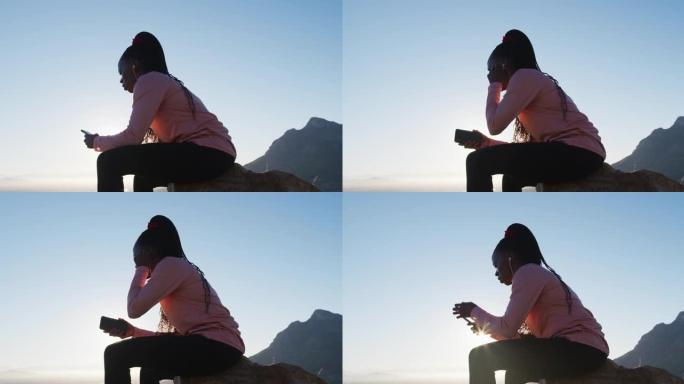 日落时分，在乡村使用智能手机坐在岩石上户外锻炼的非洲裔美国妇女