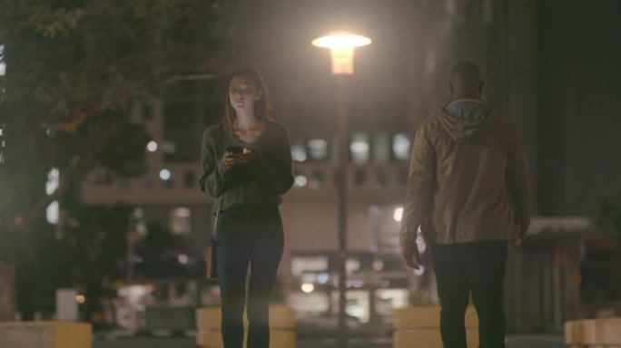 4k视频片段，一名妇女晚上在外面散步时使用手机