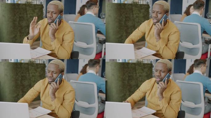 非裔美国商人在手机上讲话并在共享办公室中使用笔记本电脑