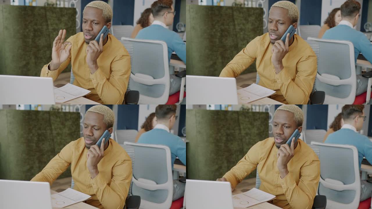非裔美国商人在手机上讲话并在共享办公室中使用笔记本电脑