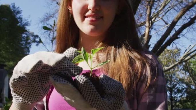 微笑的高加索少女在花园里工作，戴着手套并检查植物