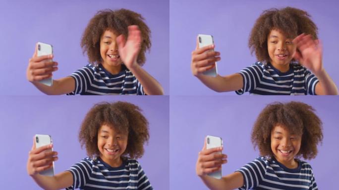 微笑男孩在紫色工作室背景下在视频通话手机上挥手的工作室镜头-慢动作拍摄