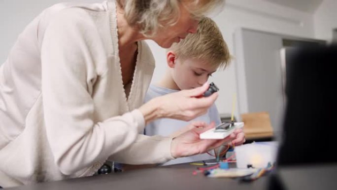 孙子与祖母组装电子元件在家中一起建造机器人