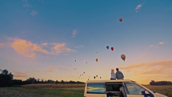 夫妇坐在面包车上看着农村地区的热气球