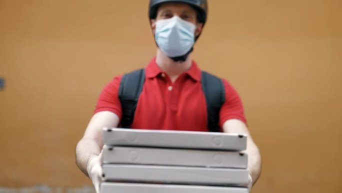 一位年轻的披萨送货快递员的肖像，戴着防护口罩和手套，对他在相机中的工作感到满意。快递，送货上门，电子