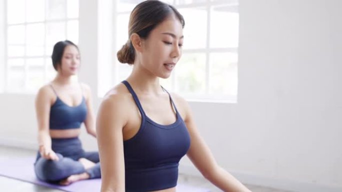 年轻的亚洲运动型有魅力的人与教练一起练习瑜伽课。亚洲妇女团体在健身工作室锻炼健康的生活方式。