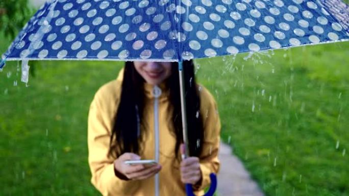 SLO MO年轻女子在雨中使用智能手机玩得开心