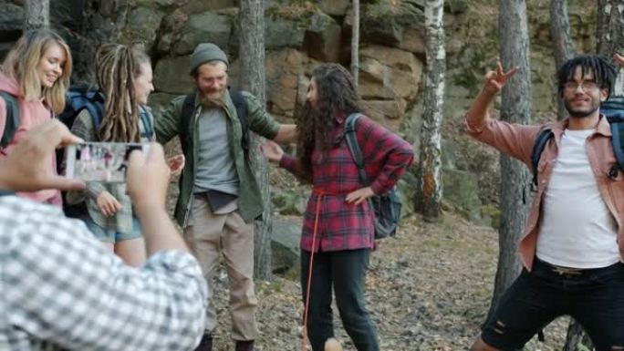 顽皮的游客在森林里用智能手机相机拍照时，开心地摆姿势大笑