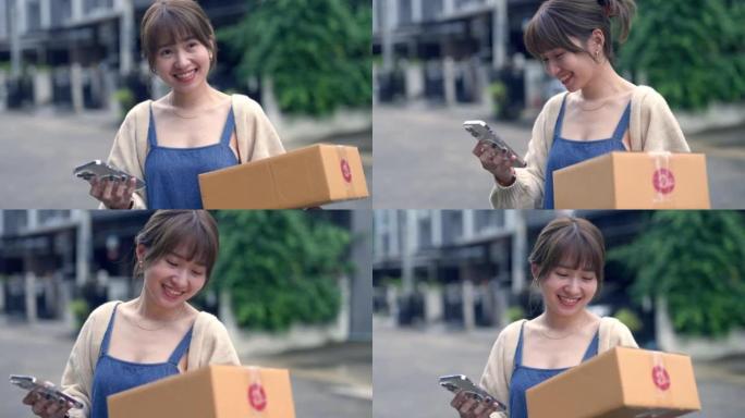 年轻的亚洲妇女在家中携带一堆送货箱时在手机上阅读信息